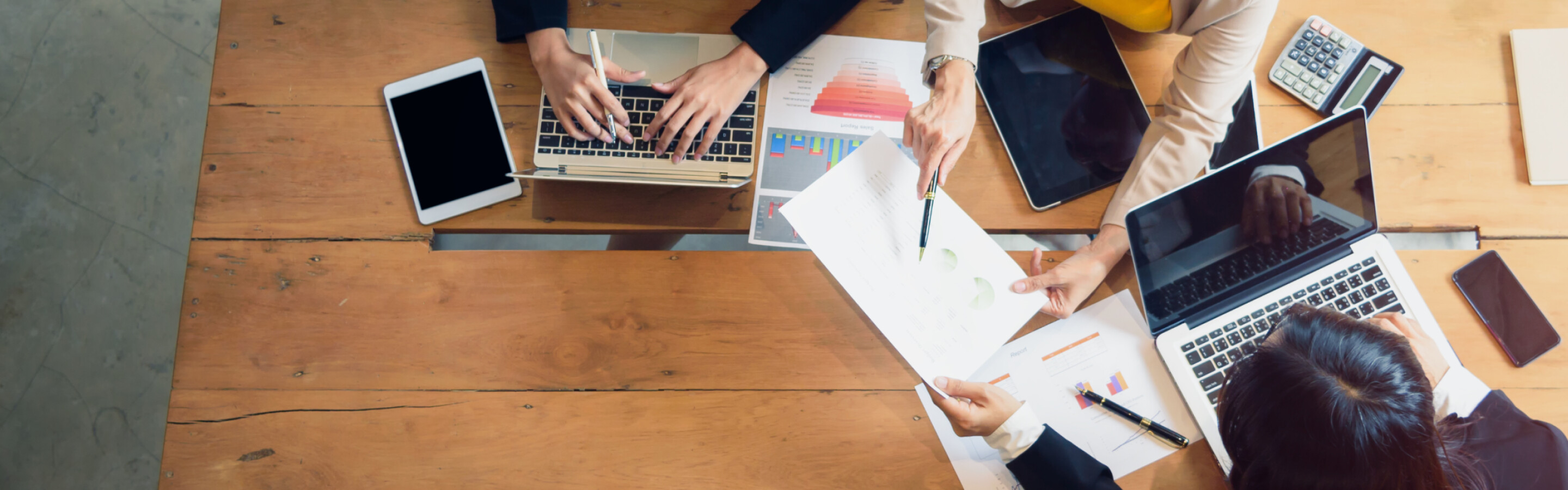 A photo looking down at a table with people working with notebooks and laptops